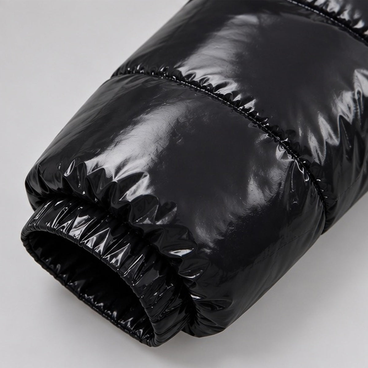Close-up van glanzende zwarte gewatteerde mouw met geplooide elastische manchet | Boutique Moda