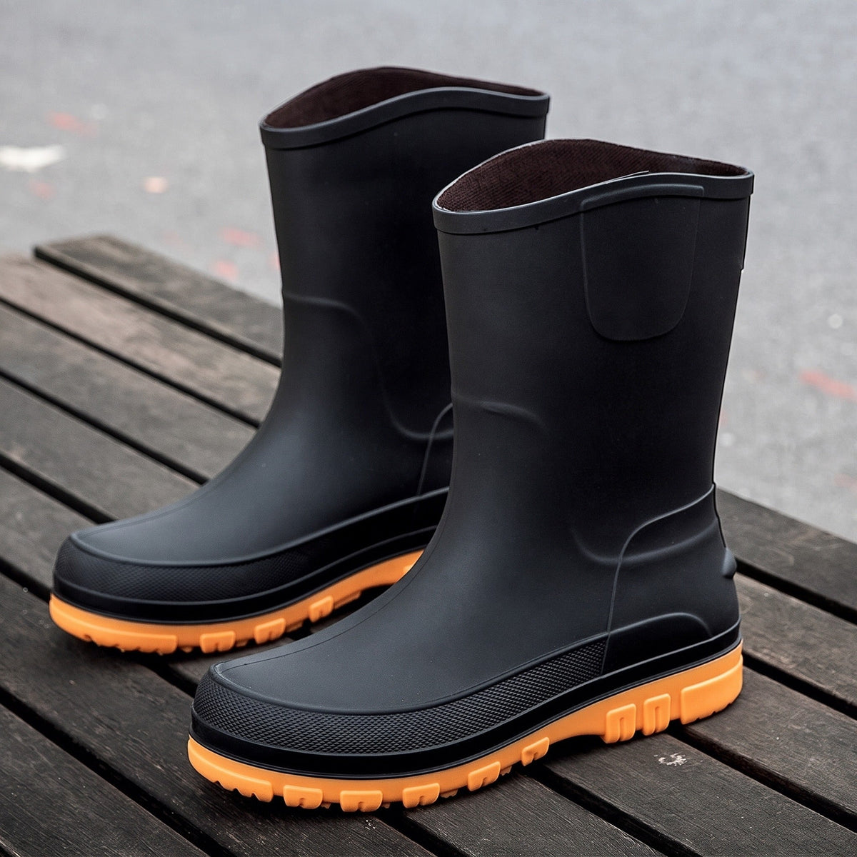 Zwarte halfhoge regenlaarzen met oranje zool, los staand op houten vlonder | Boutique Moda