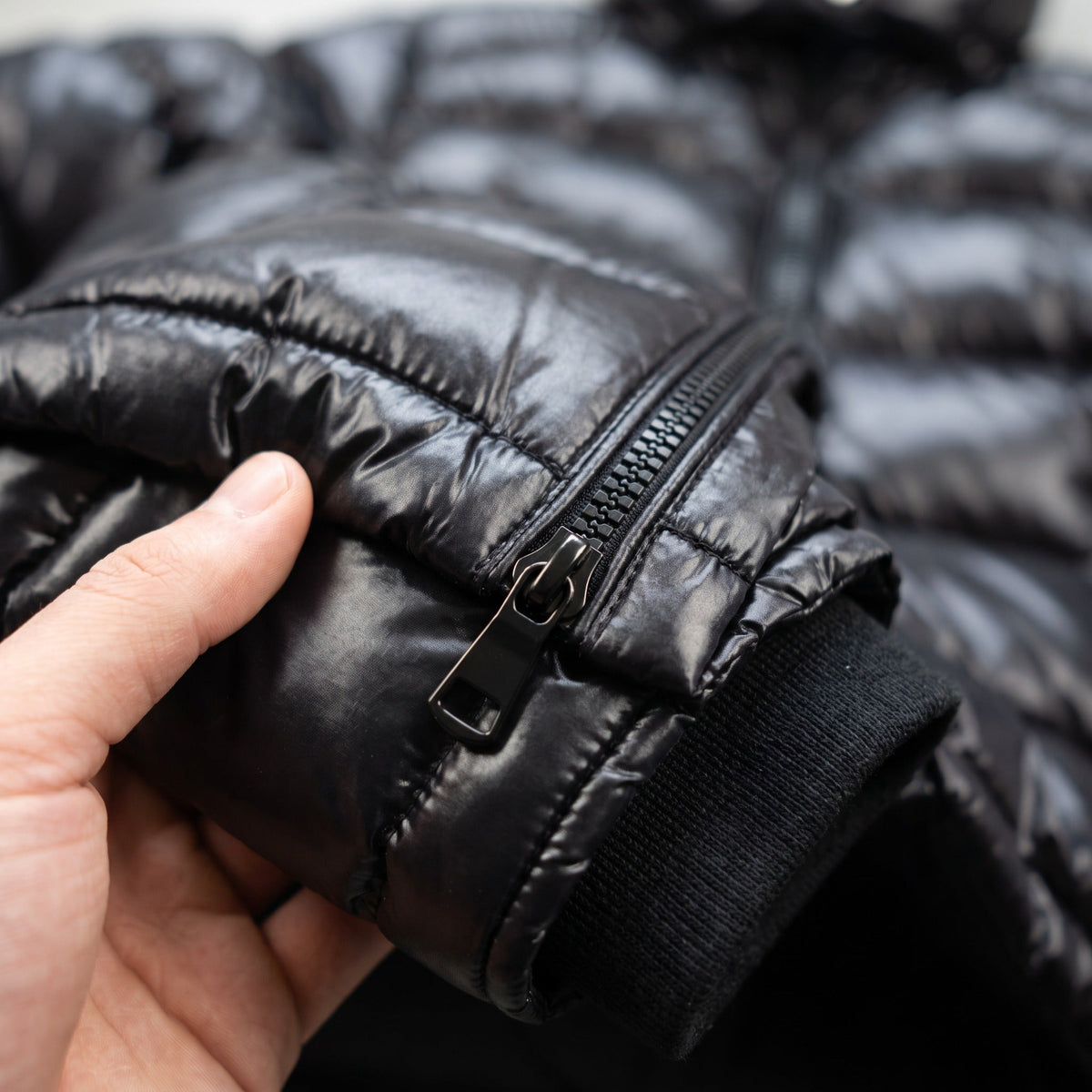 Zwarte glanzende gewatteerde jas met rits, van dichtbij gedragen door persoon | Boutique Moda