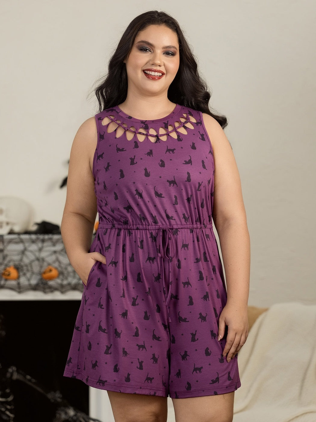 Vrouw in de pruimkleurige playsuit met kattenprint thuis met Halloween decoratie