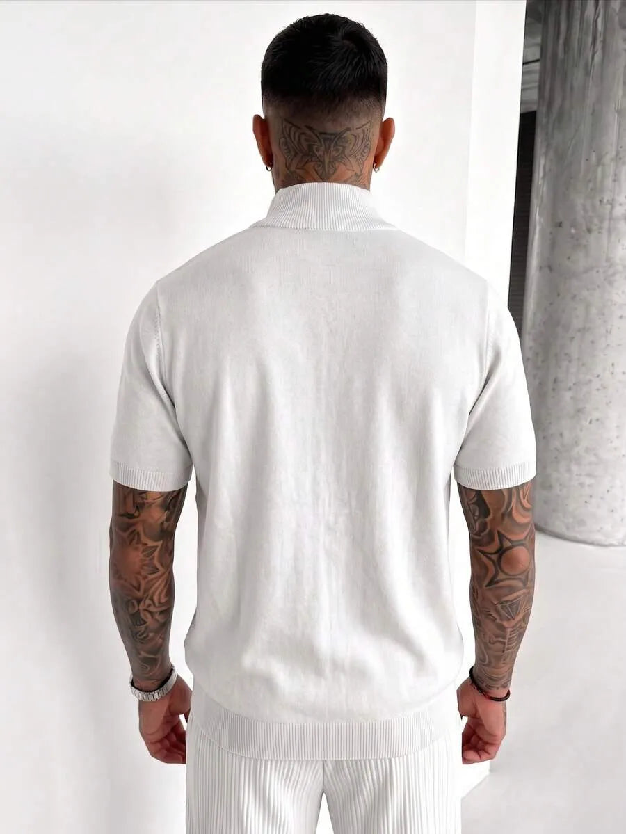 Man seen from behind wearing a white knit half-zip polo shirt with short sleeves and matching trousers, with tattoos visible on both arms and neck.