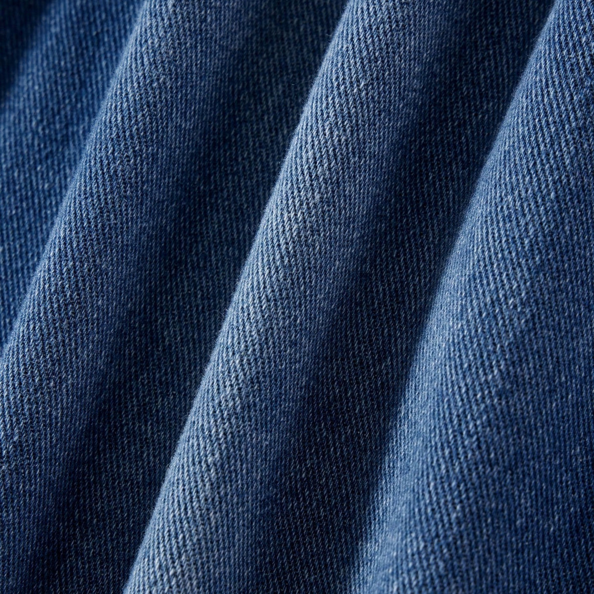 Close-up van blauwe denim stof met diepe plooien en zichtbare textielstructuur | Boutique Moda