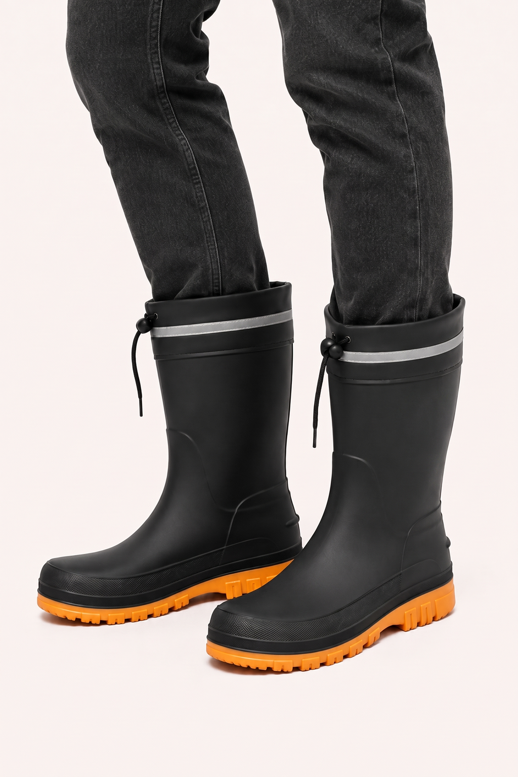 Zwarte regenlaarzen met oranje zool, gedragen door een persoon | Boutique Moda