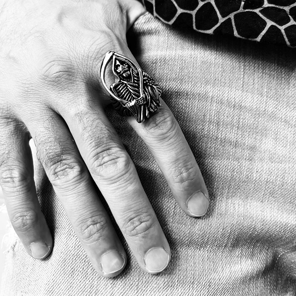 Zilverkleurige ring met zeis-motief gedragen aan vinger, zwart-wit foto | Boutique Moda