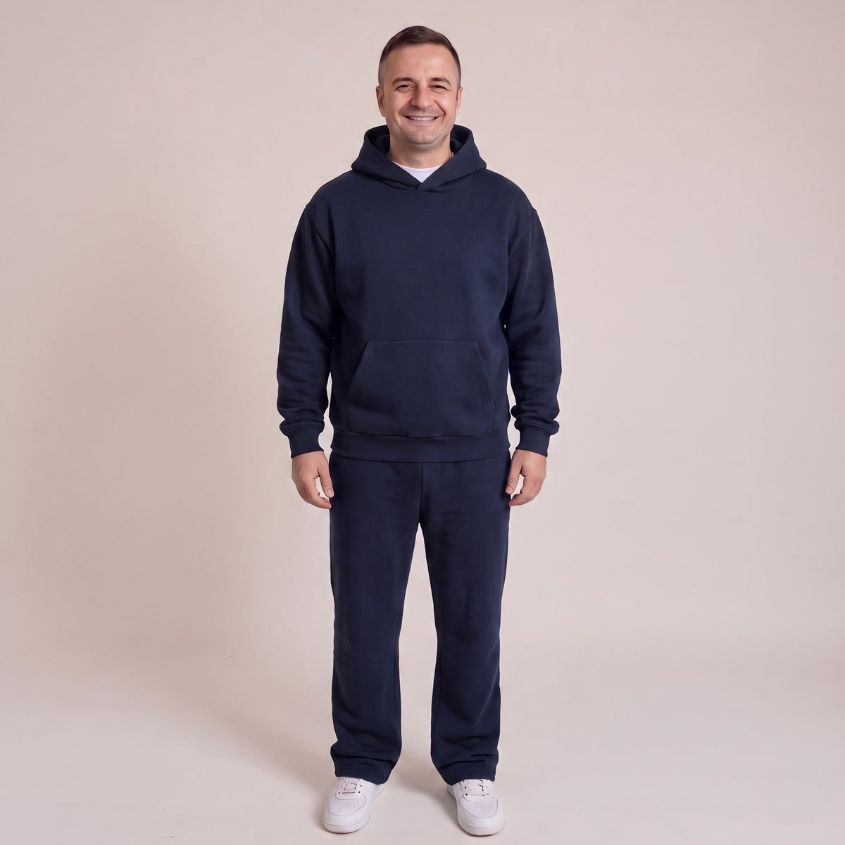 Man draagt donkerblauw joggingpak met hoodie en witte sneakers | Boutique Moda