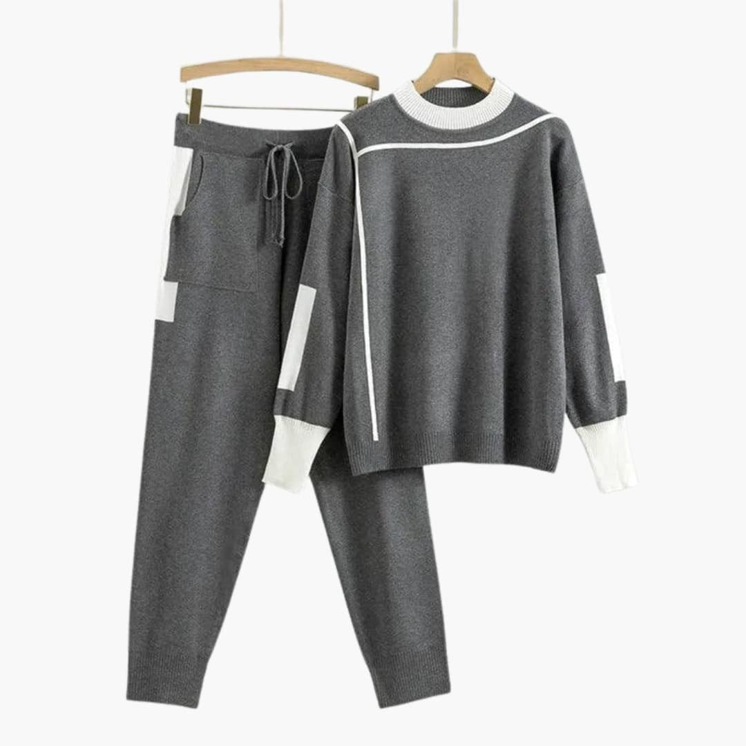 Grijs gebreid joggingpak voor dames met witte contrastbiezen, trui en broek aan een hanger