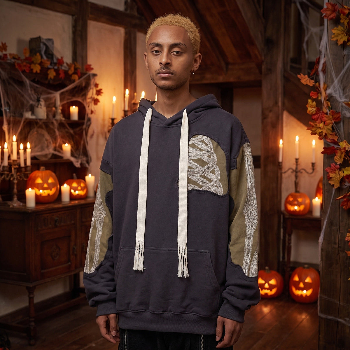 Donkergrijze patchwork hoodie met skeletprint mouwen, gedragen door man binnenshuis | Boutique Moda