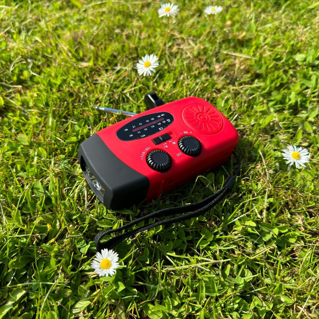 Rode noodradio met zaklamp en antenne ligt in gras | Boutique Moda