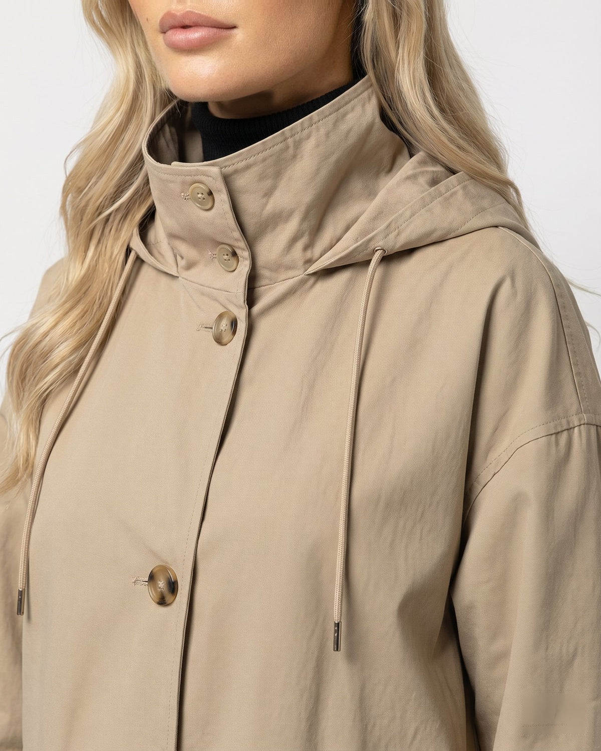 Close-up van de opstaande kraag met capuchon en koordjes van de beige lange parka jas | Boutique Moda