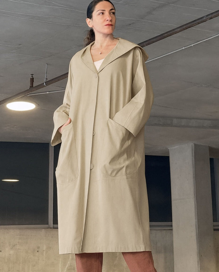 Beige oversized regenjas met capuchon, gedragen door vrouw binnenshuis | Boutique Moda