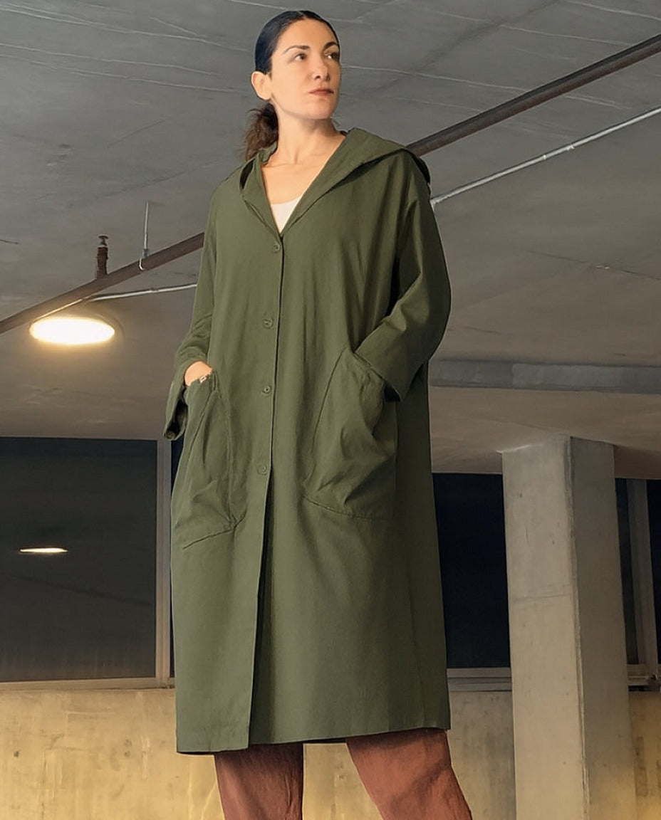 Groene oversized regenjas met capuchon en zakken, gedragen door vrouw binnenshuis | Boutique Moda