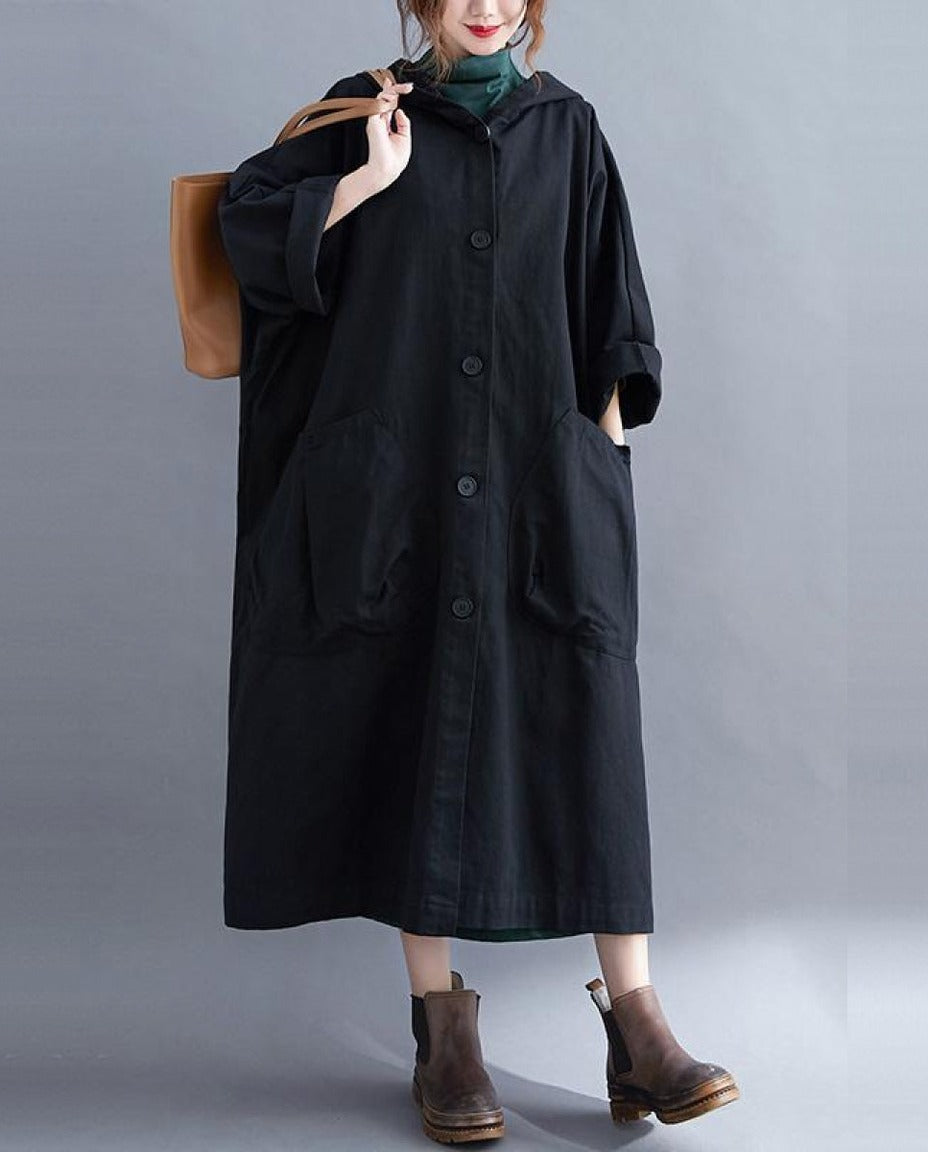 Zwarte lange oversized regenjas met capuchon, gedragen door vrouw met tas | Boutique Moda