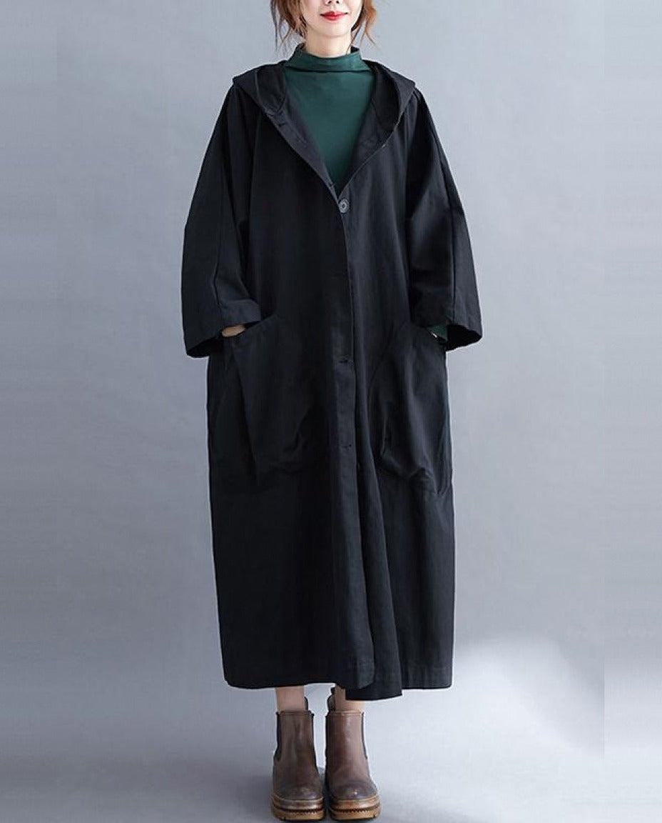 Zwarte lange oversized regenjas met capuchon, gedragen door model met laarzen | Boutique Moda