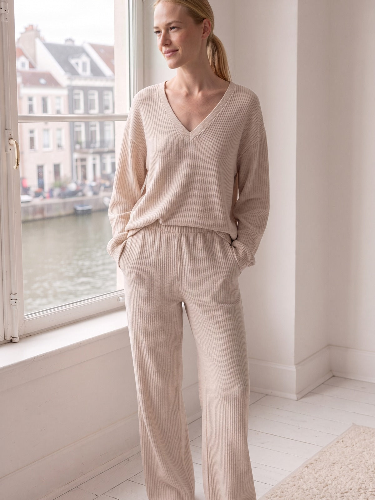 Vrouw in een beige geribde loungewearset met V-hals in een Amsterdams appartement
