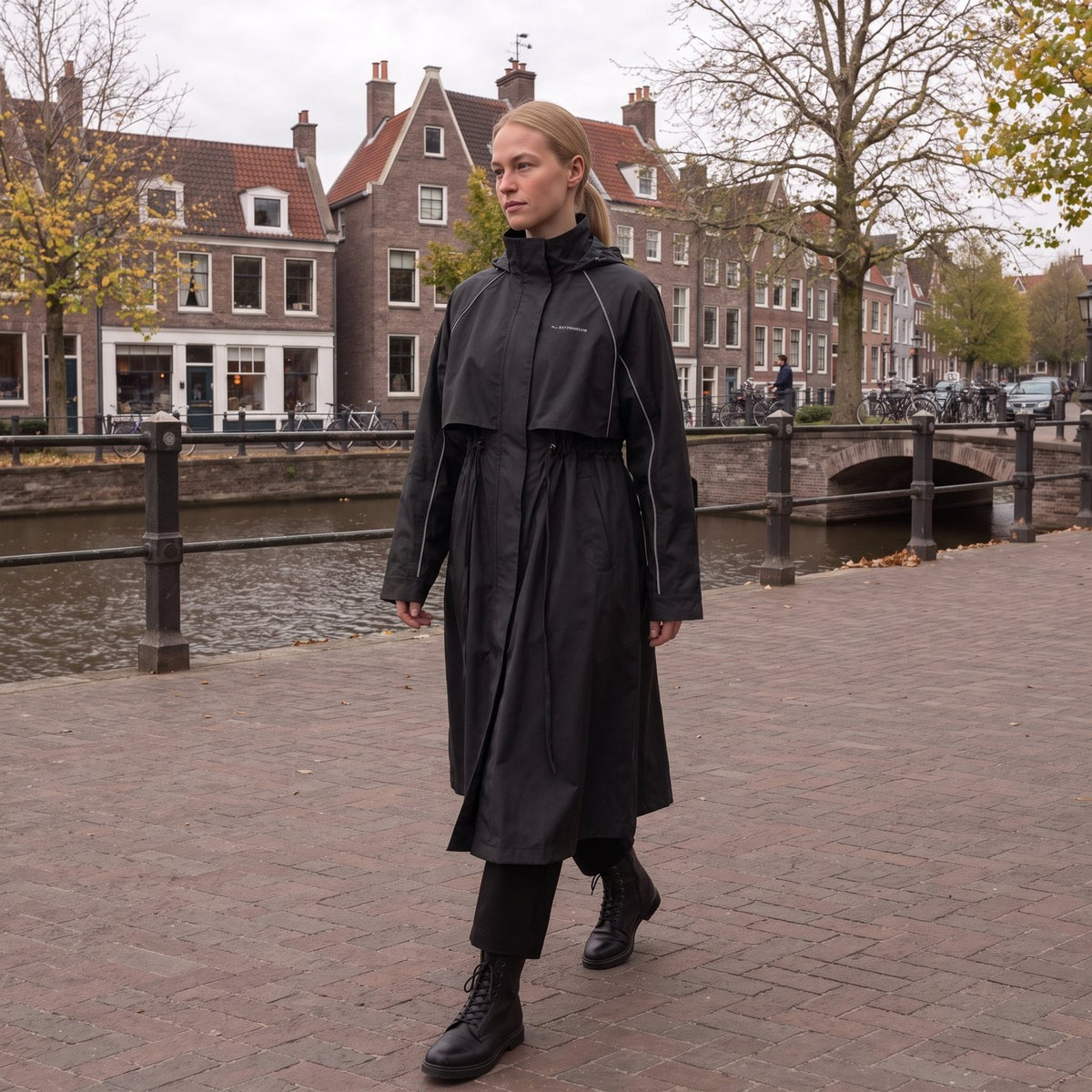 Vrouw in de lange zwarte regenjas aan een Nederlandse gracht