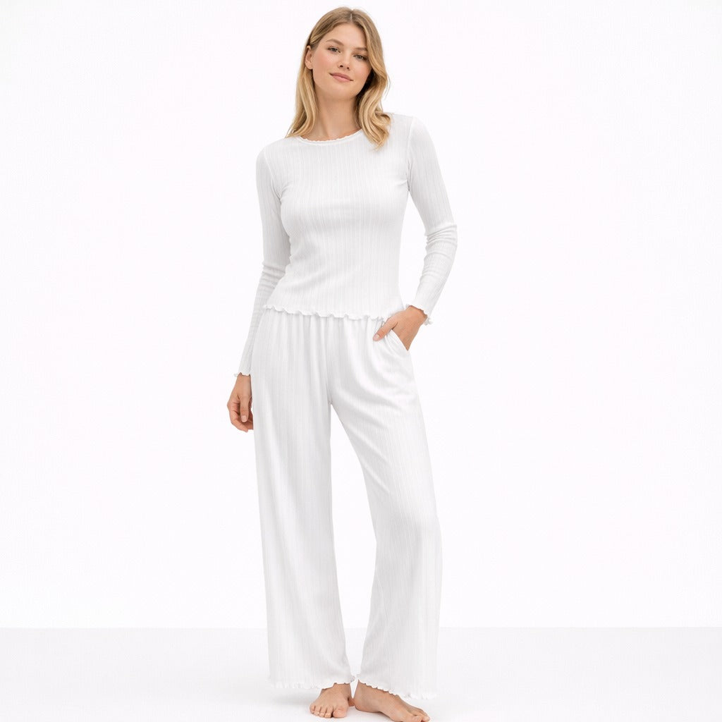 Vrouw in een witte pointelle pyjama set met lange mouwen en wijde broek