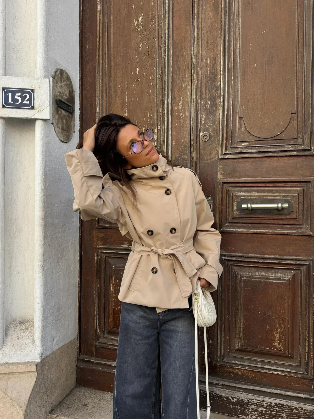 Beige korte trenchcoat bij een houten deur | Boutique Moda