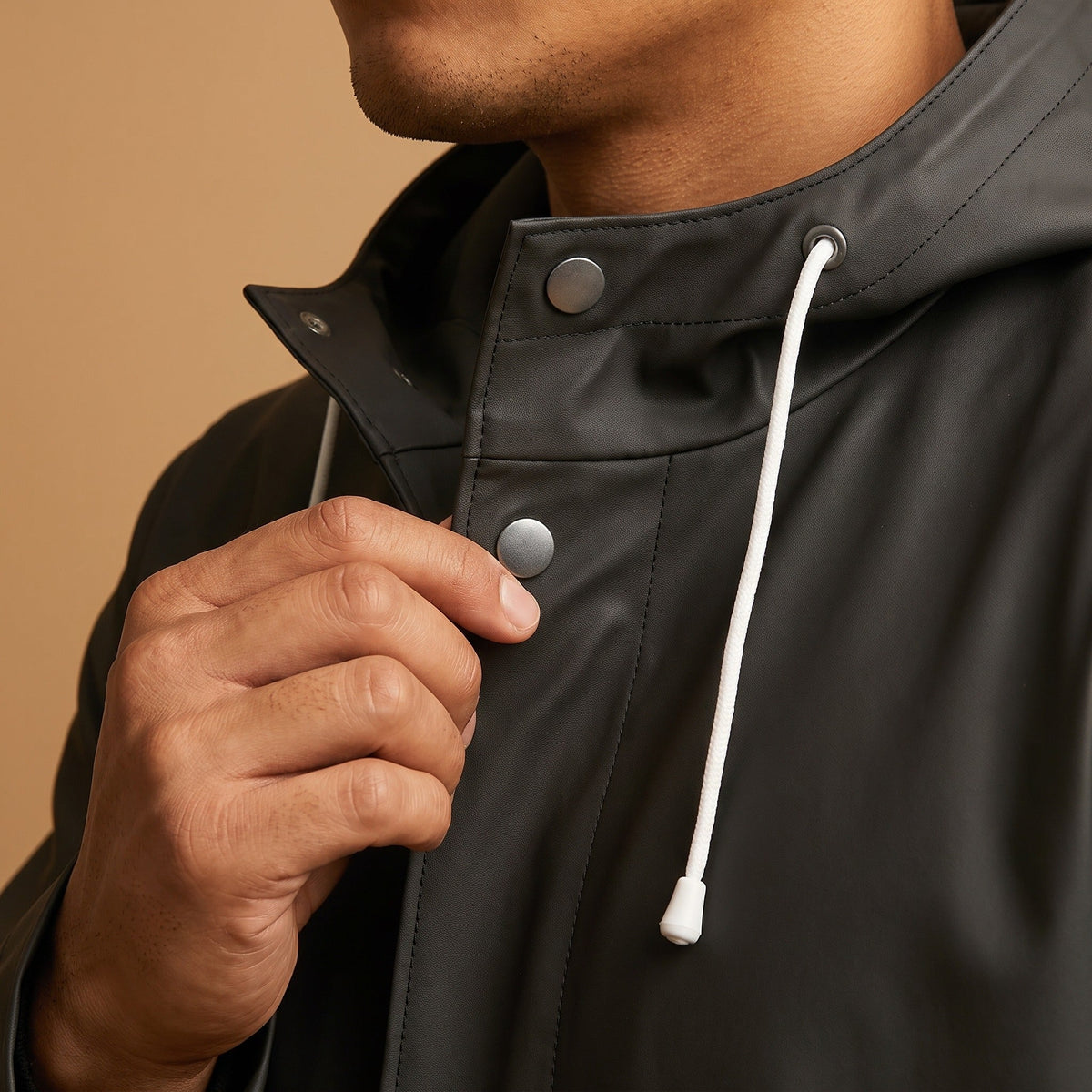 Zwarte regenjas met capuchon en drukknoop, gedragen door persoon, detailopname | Boutique Moda