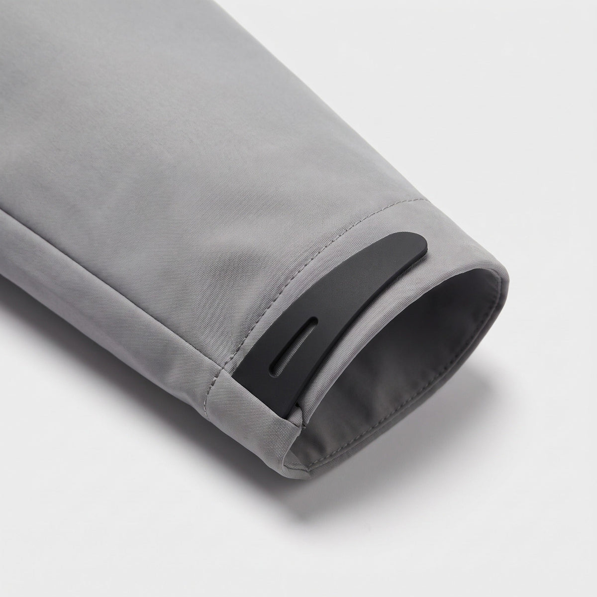 Grijze regenjas mouwdetail met zwarte klittenband sluiting, close-up studiofoto | Boutique Moda