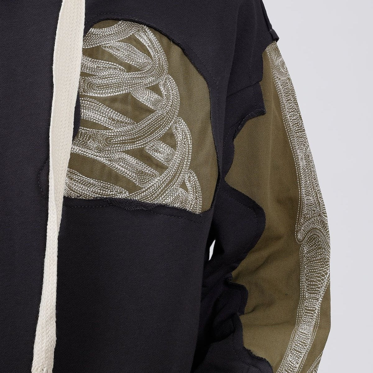 Close-up zwart en kaki hoodie met geborduurd botmotief, gedragen door persoon | Boutique Moda