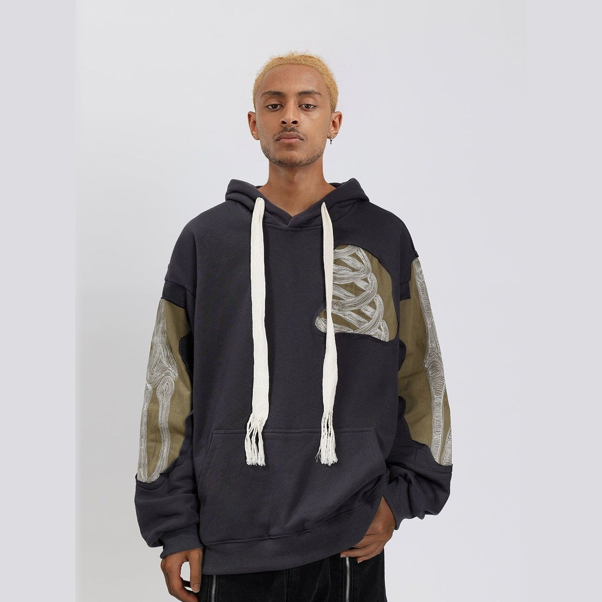 Donkere oversized hoodie met kaki patchwork en geborduurd motief, gedragen door man | Boutique Moda
