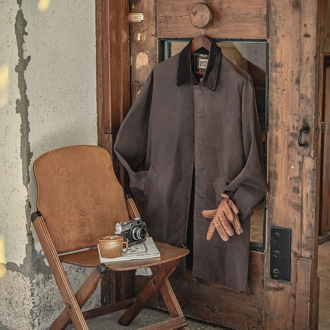 Bruine jas met corduroy kraag hangend aan houten deur, naast stoel | Boutique Moda