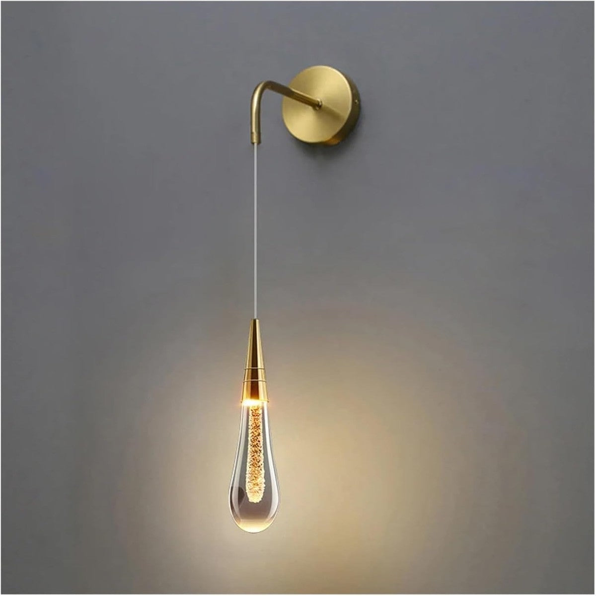 Gouden wandlamp met waterdruppelvormig glas, aan tegen een grijze muur | Boutique Moda