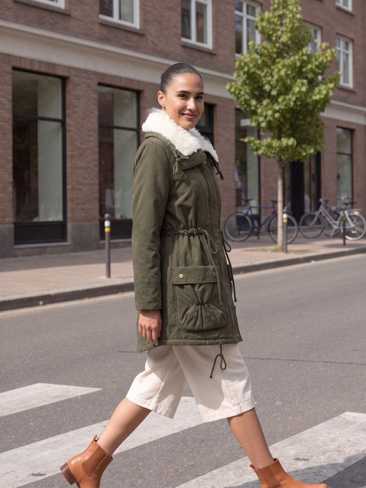 Vrouw in een olijfgroene winterparka met teddykraag die in Rotterdam oversteekt