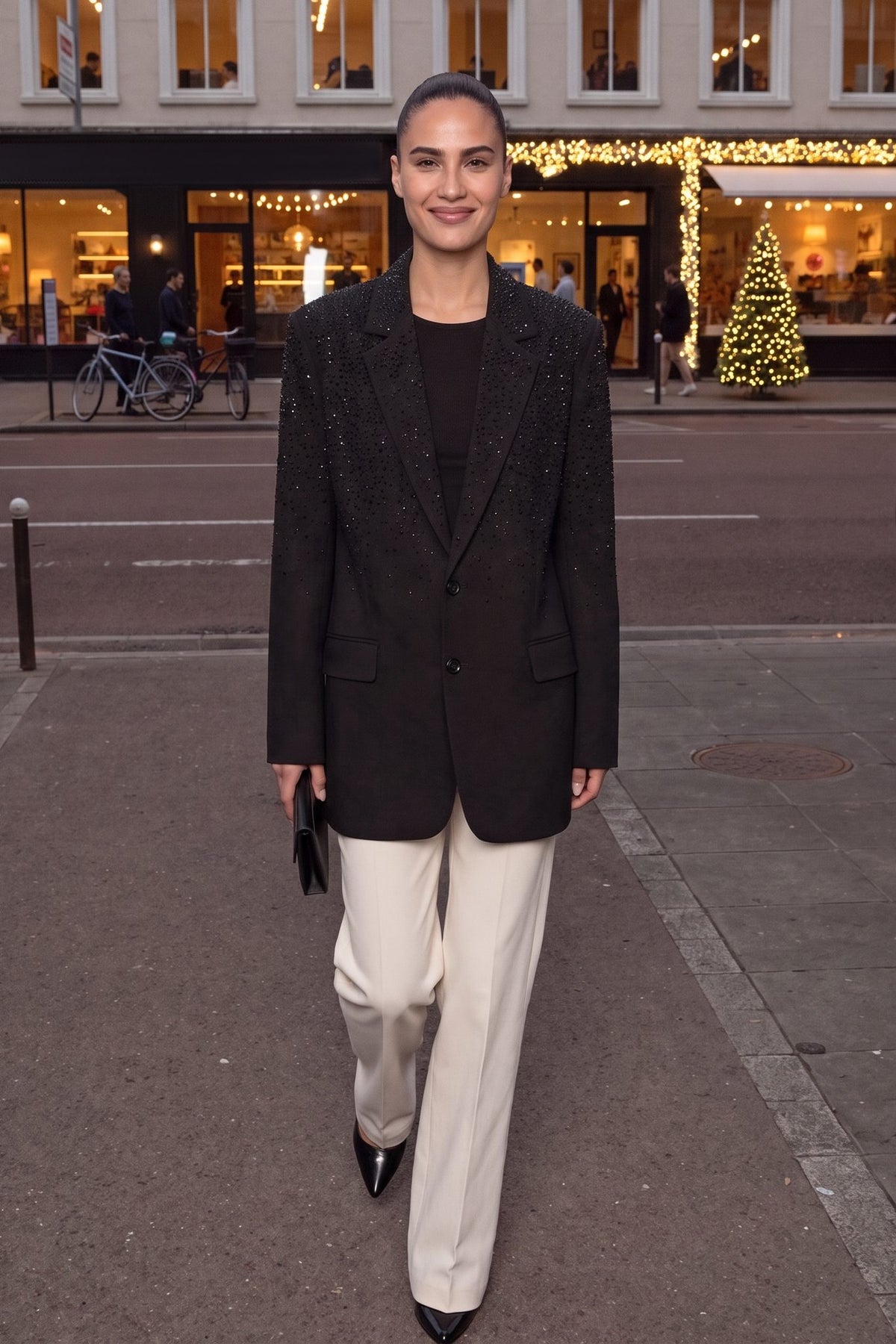 Vrouw draagt zwarte oversized blazer met strass steentjes in een winkelstraat met kerstverlichting | Boutique Moda