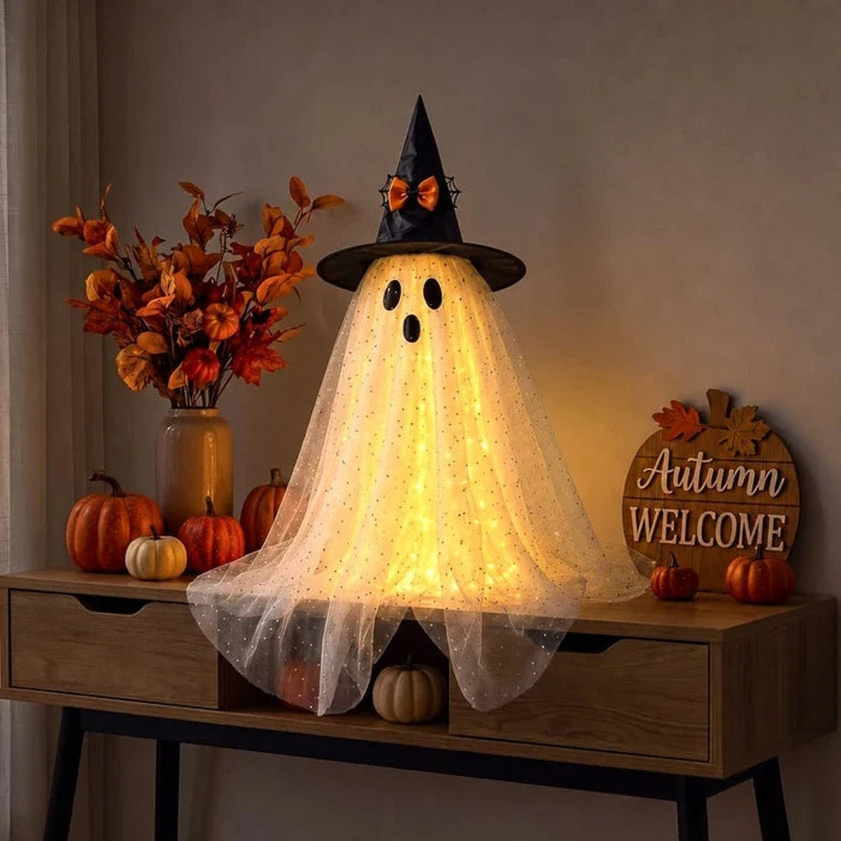 Lichtgevend spookje van tule met heksenhoed op een dressoir met pompoenen