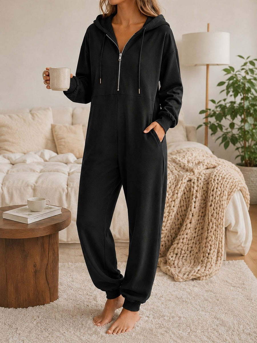 Onesie met capuchon in zwart met halve rits en zakken opzij, vooraanzicht in de slaapkamer
