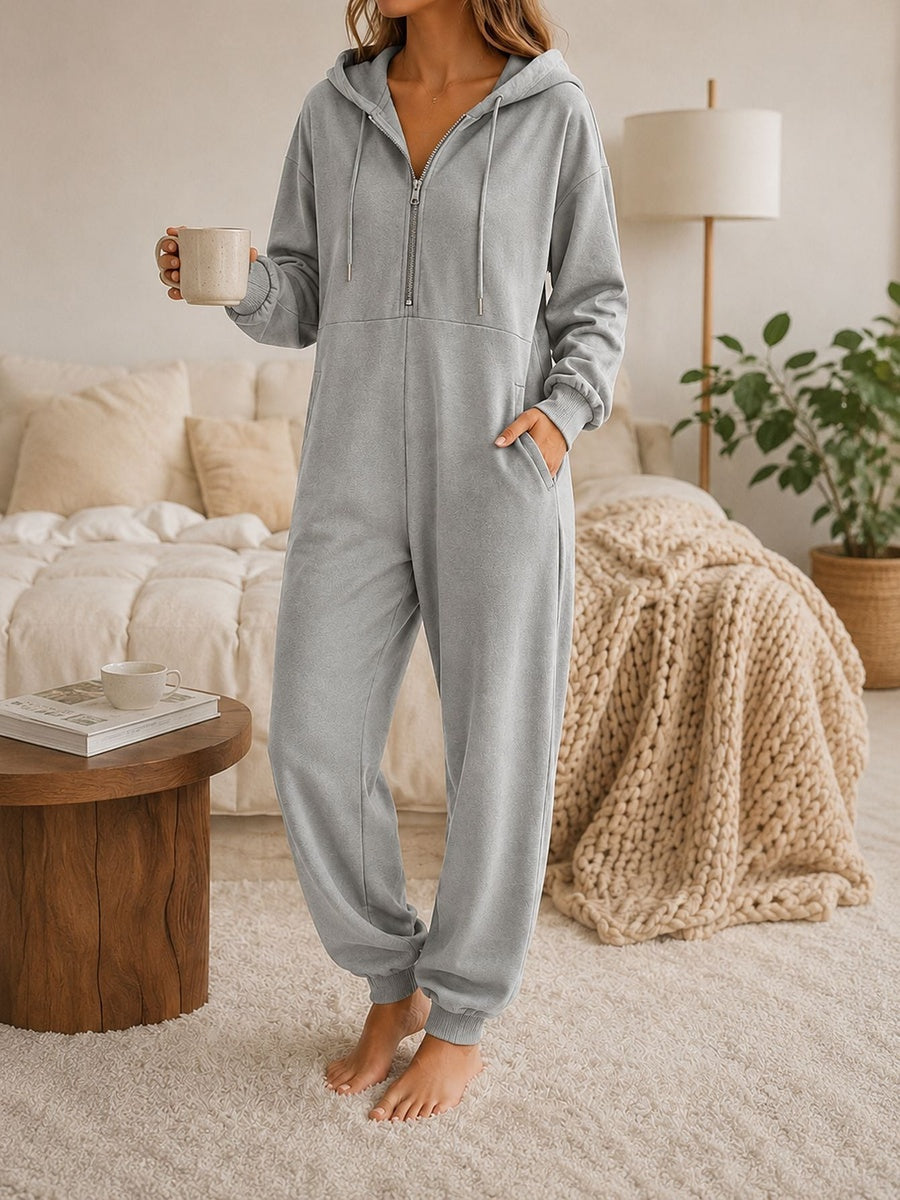 Onesie met capuchon in grijs met halve rits en zakken opzij, vooraanzicht in de slaapkamer