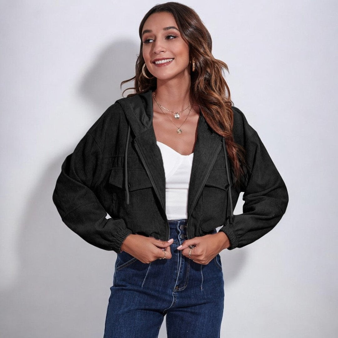 Vrouw draagt korte zwarte corduroy jas met capuchon over een wit topje en hoge jeans | Boutique Moda