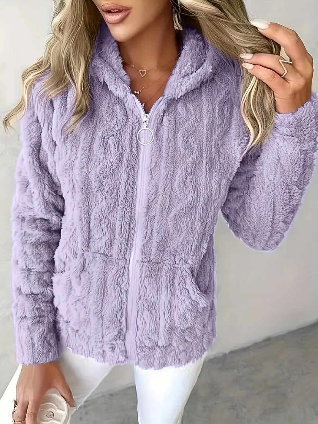 Vrouw draagt een lila teddyvest met zilveren ringtrekker en een witte broek, hand in het haar | Boutique Moda