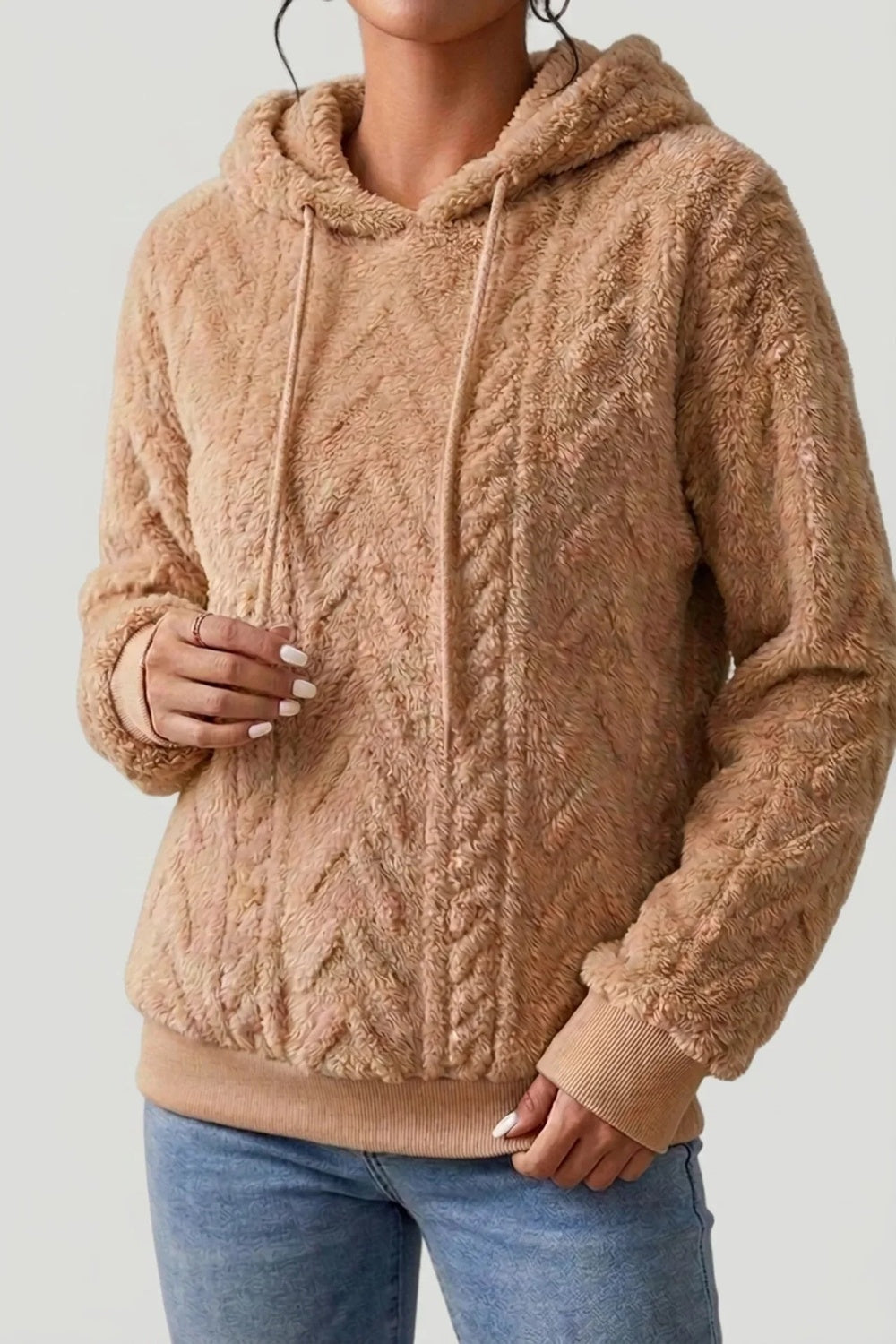 Vrouw in een karamelkleurige teddytrui met capuchon en kabelpatroon, met een jeans | Boutique Moda