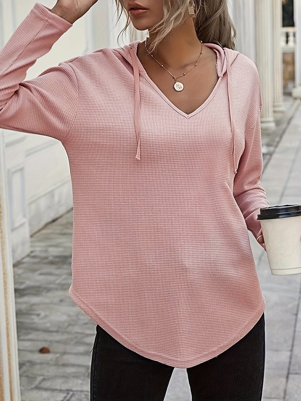 Vrouw met een koffiebeker in een oudroze hoodie met V-hals, hand in het haar | Boutique Moda