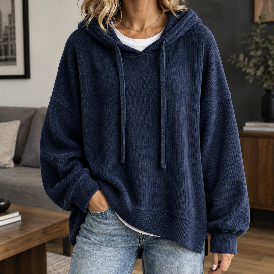 Vrouw in een marineblauwe gebreide trui met capuchon over een wit T-shirt, hand in de broekzak | Boutique Moda