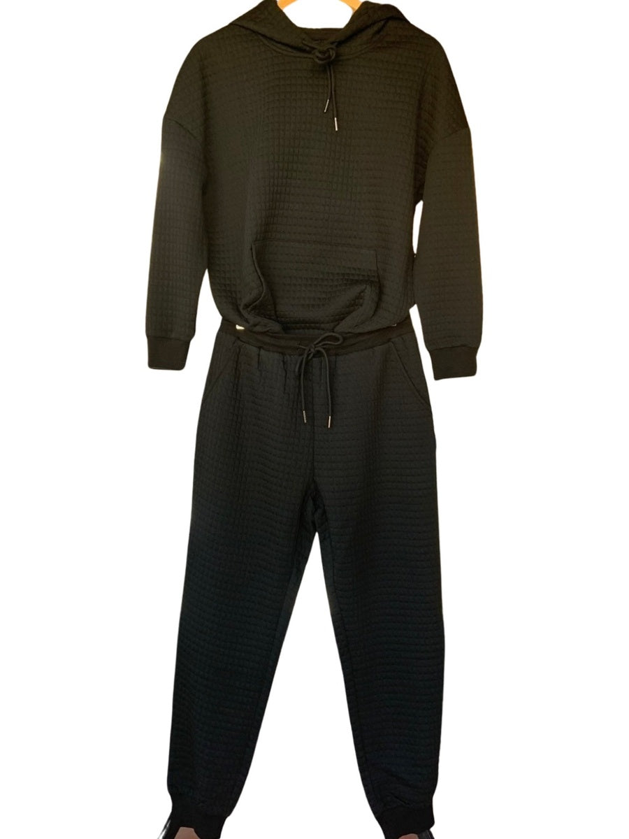 Joggingpak met wafelstructuur in zwart, hoodie met koord en joggingbroek aan een hanger