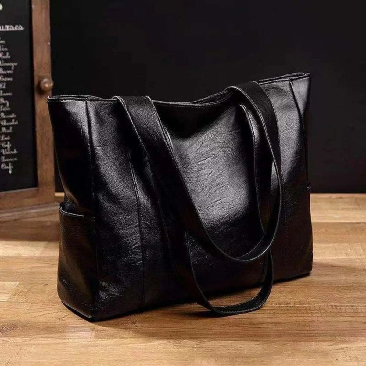 Zwarte leren shoppertas met dubbele hengsels, vrijstaand op houten ondergrond | Boutique Moda