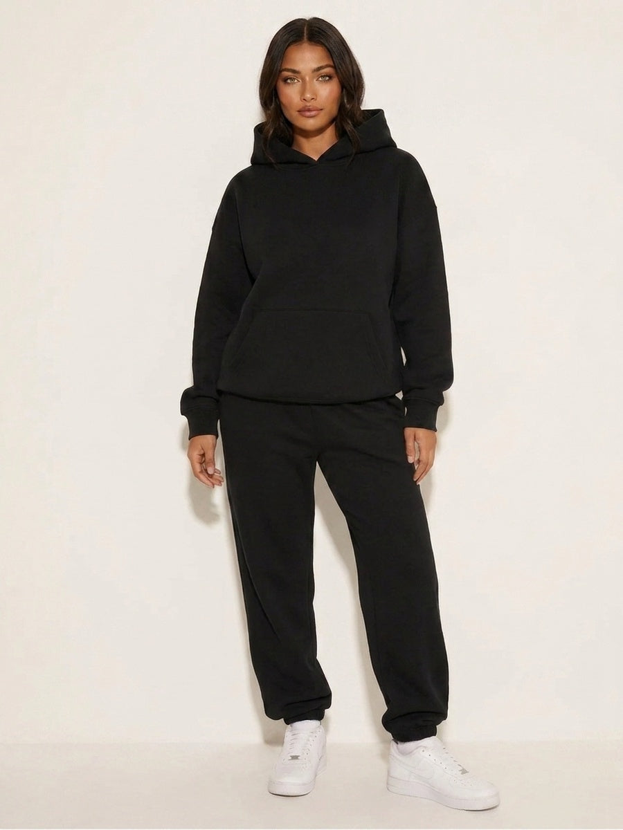Vrouw draagt zwarte oversized hoodie met bijpassende joggingbroek en witte sneakers | Boutique Moda