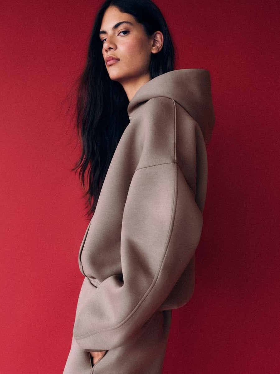 Taupe oversized hoodie gedragen door vrouw tegen rode achtergrond | Boutique Moda