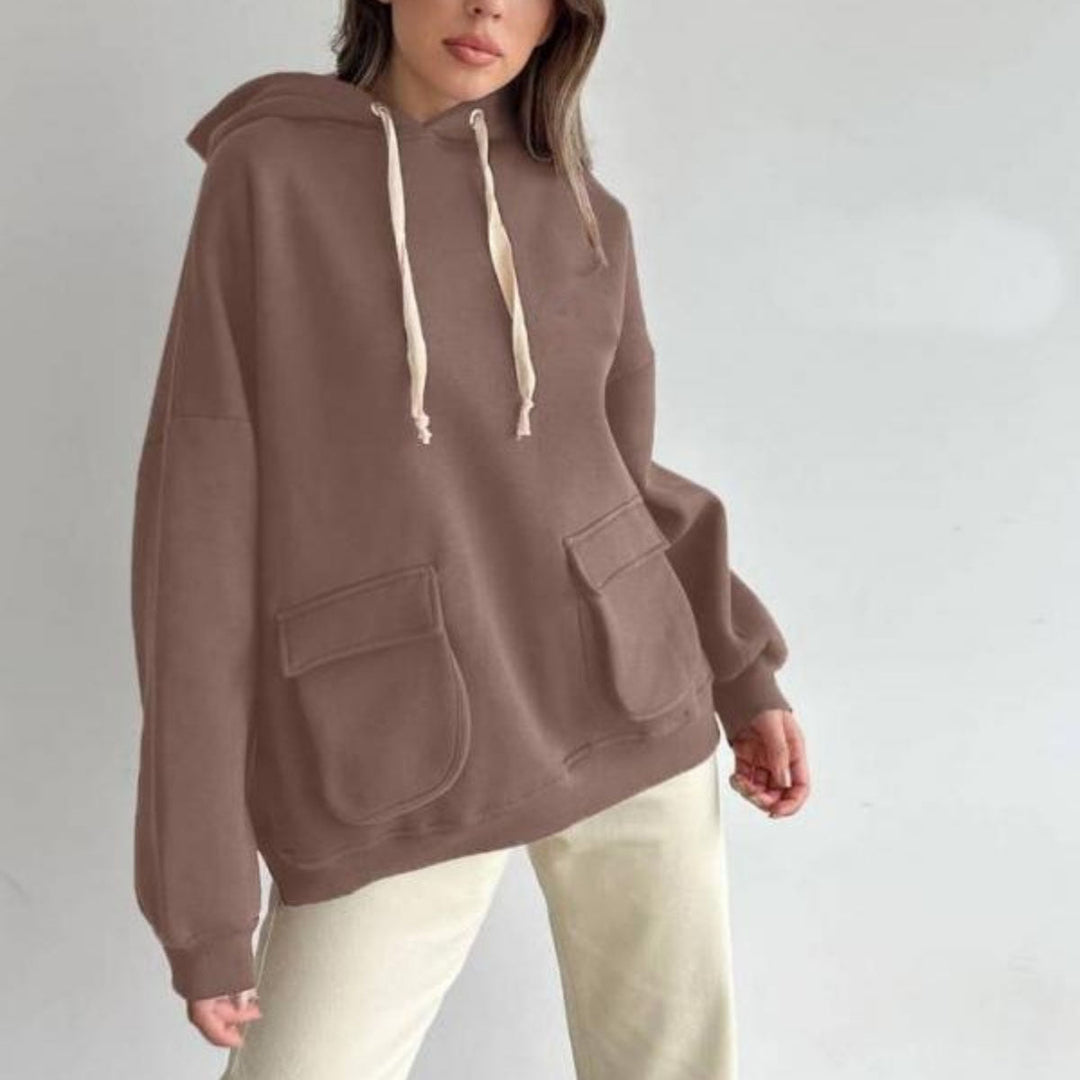 Vrouw in een mokkakleurige oversized hoodie met lichte koorden en een lichte broek | Boutique Moda