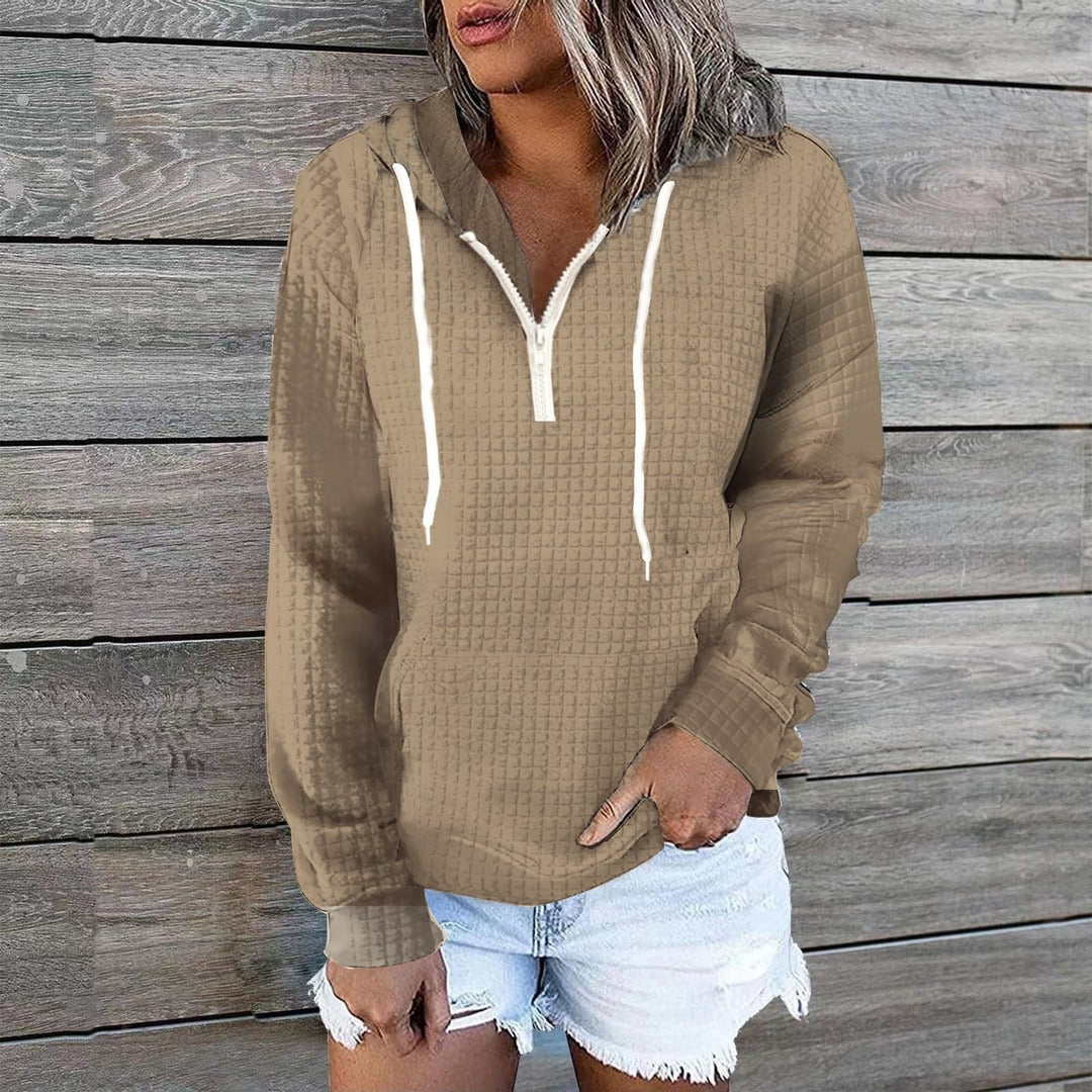 Vrouw in een khaki hoodie met halve rits bij de hals, voor een houten wand | Boutique Moda