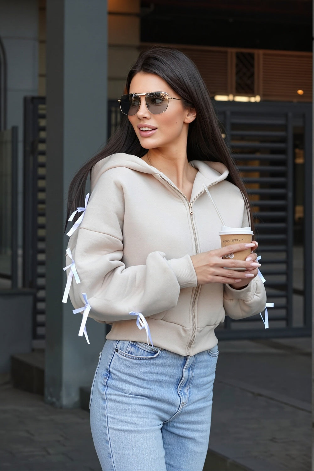Vrouw in een beige vest met een lichte jeans, strikjes langs beide mouwen | Boutique Moda
