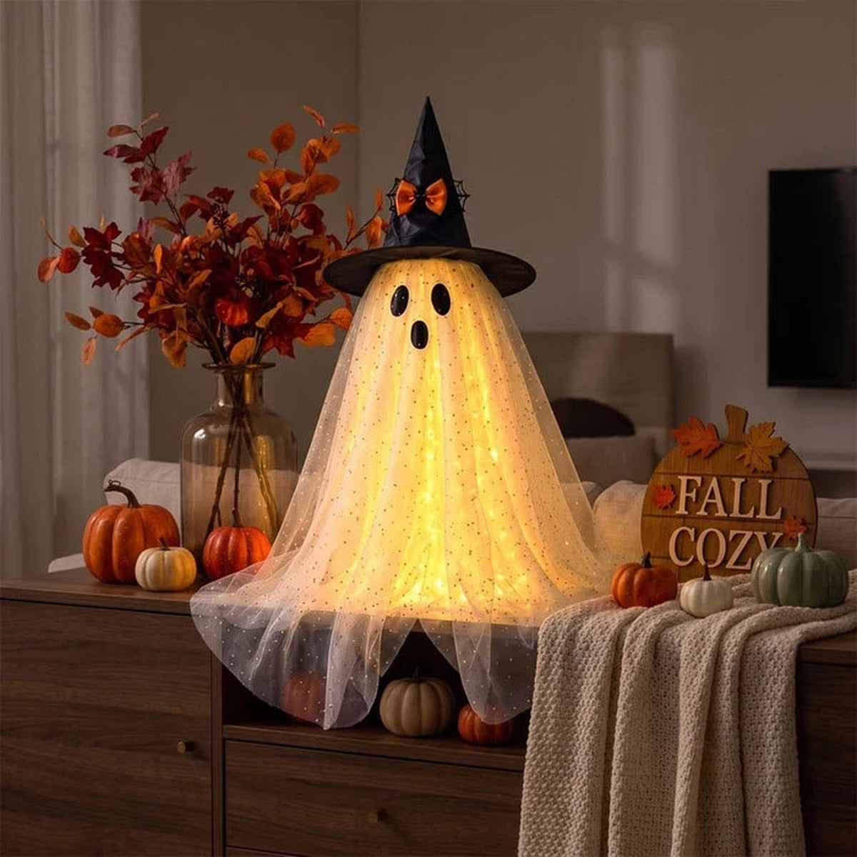 Spookje van tule met warm licht naast een vaas met herfsttakken