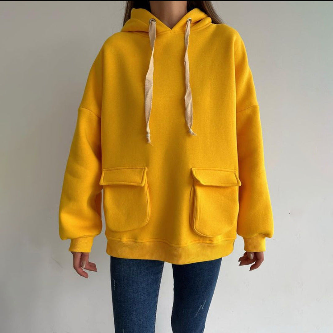 Vrouw in een mosterdgele oversized hoodie met twee klepzakken en een jeans, vooraanzicht | Boutique Moda