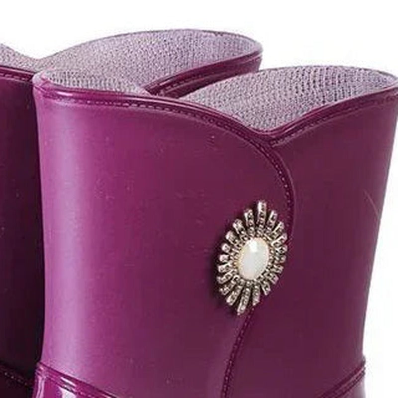 Glanzende halfhoge regenlaarzen met sierbroche in paars, close-up van de broche