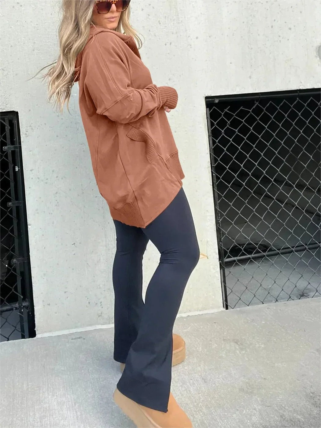Vrouw in roestbruine trui met capuchon en een donkere flared broek, zijaanzicht | Boutique Moda