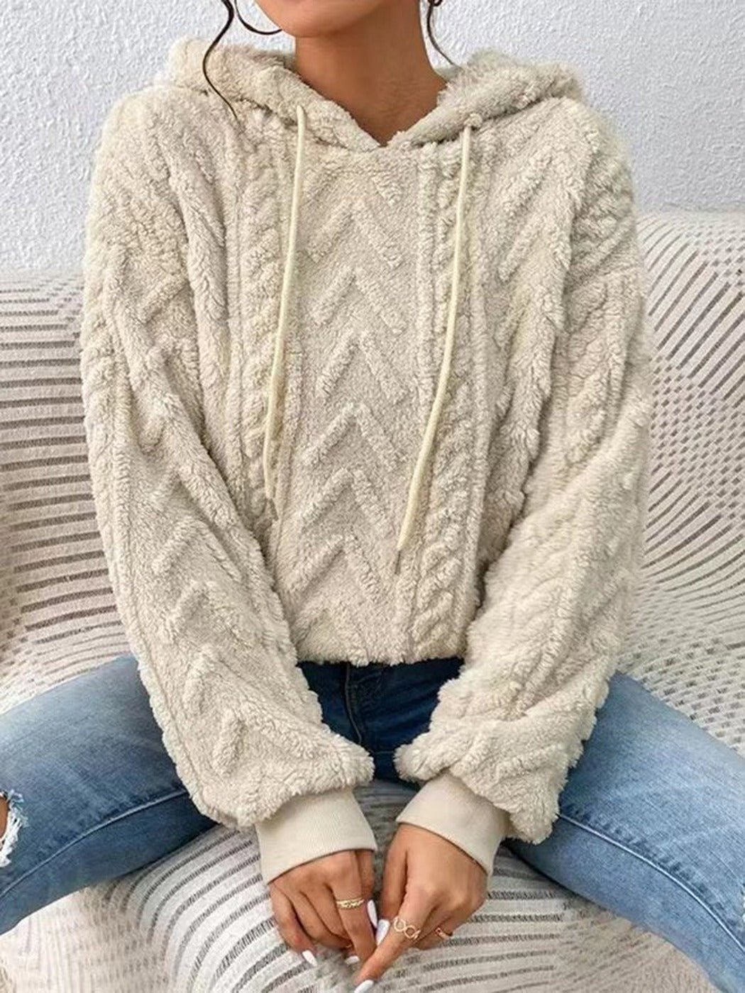 Vrouw in een crèmekleurige teddytrui met koorden en wijde mouwen, zittend op een bank | Boutique Moda