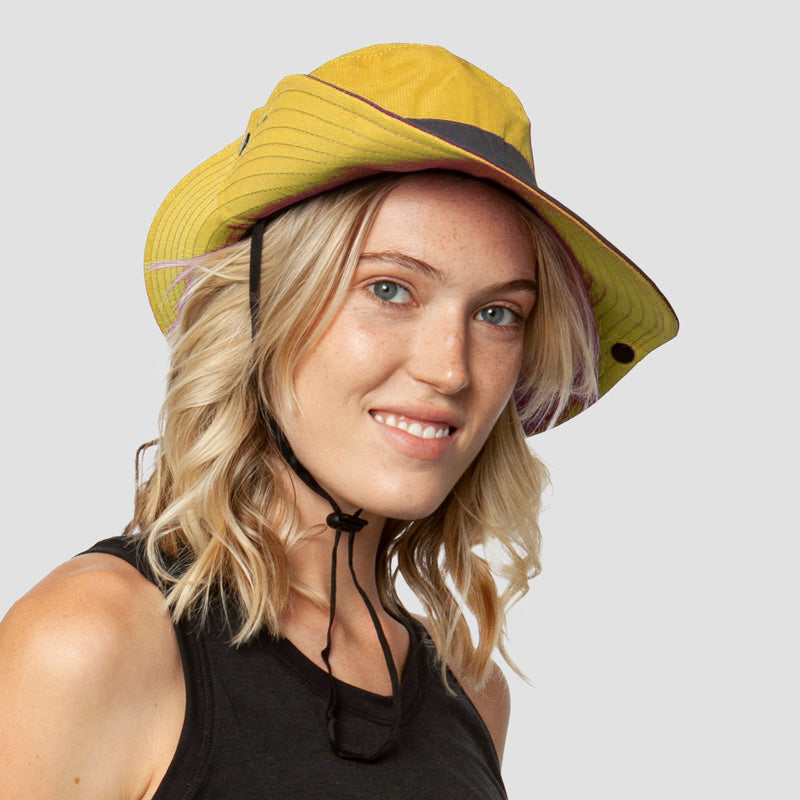 Gele stoffen zonnehoed met kinband, gedragen door glimlachende vrouw met blond haar | Boutique Moda